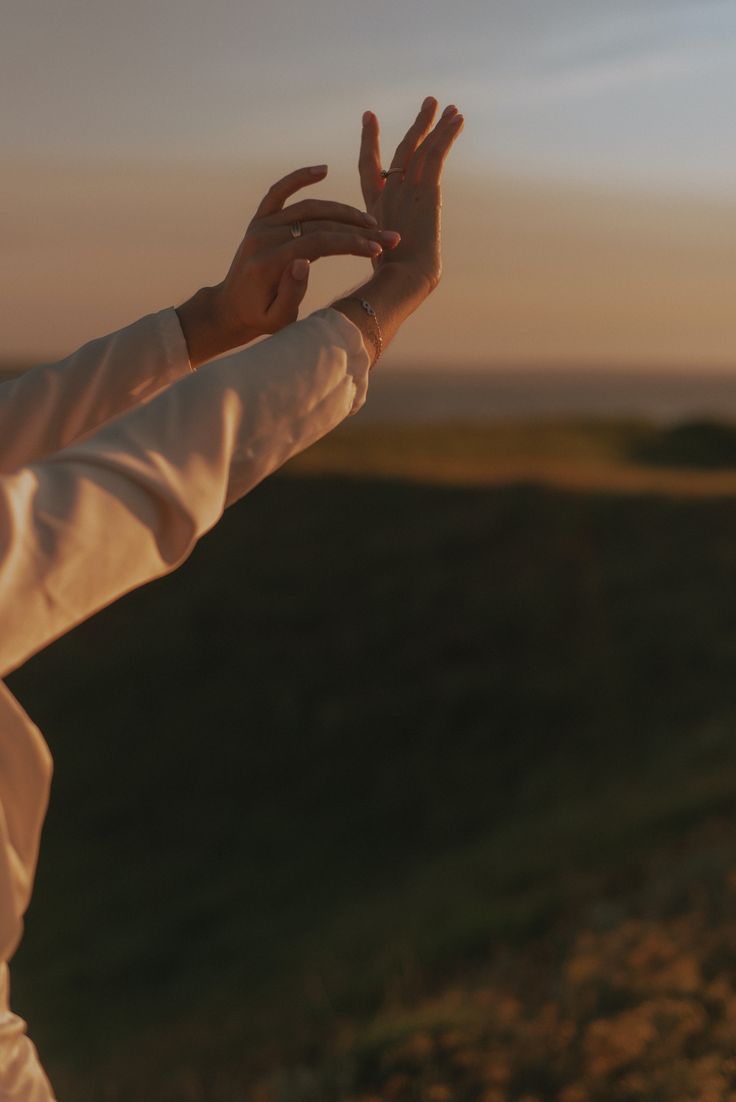 Two hands raised gracefully against a sunset sky