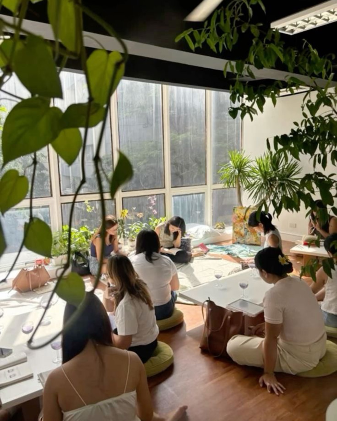 A small group seated on floor cushions in a bright, plant-filled room during a workshop
