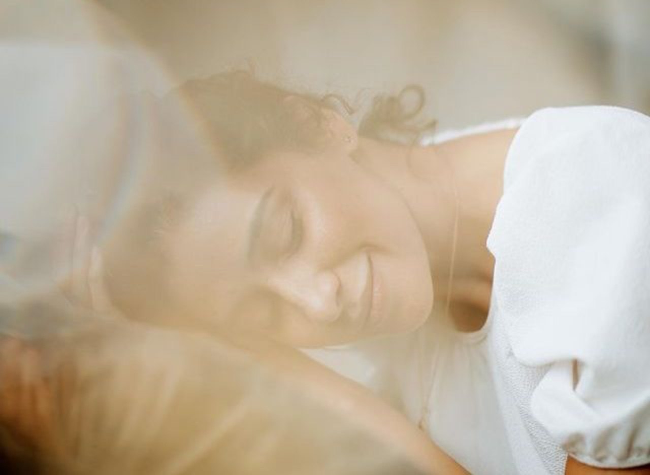 A woman resting her head and smiling with her eyes closed, in soft warm light