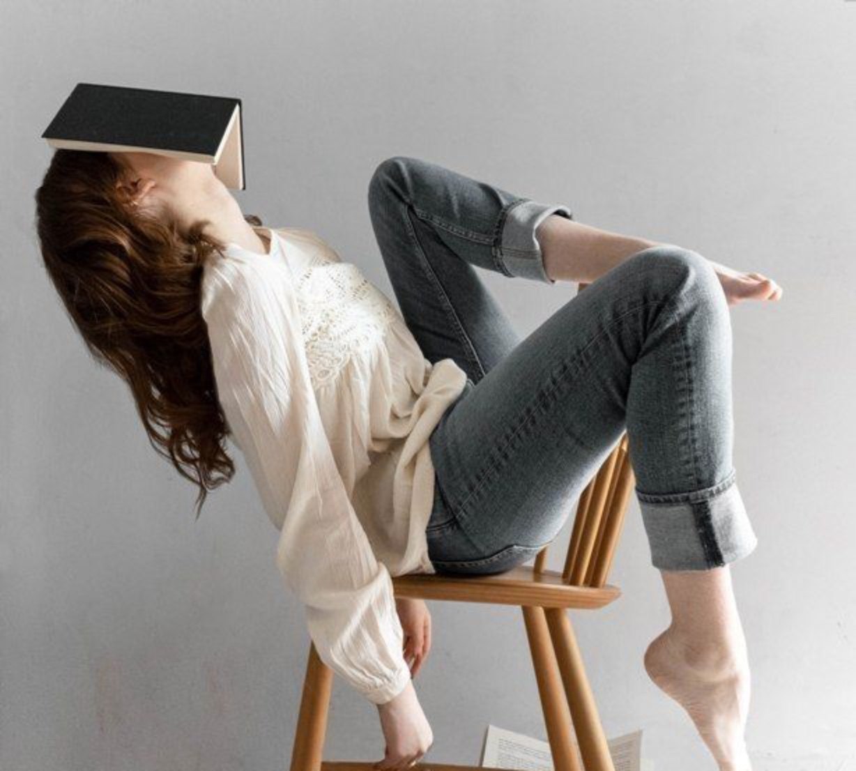 A woman slumped back in a wooden chair with an open book covering her face