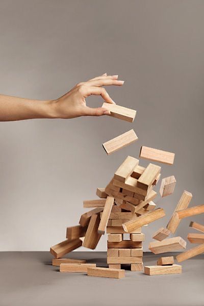 A hand pulling one block as a wooden block tower collapses